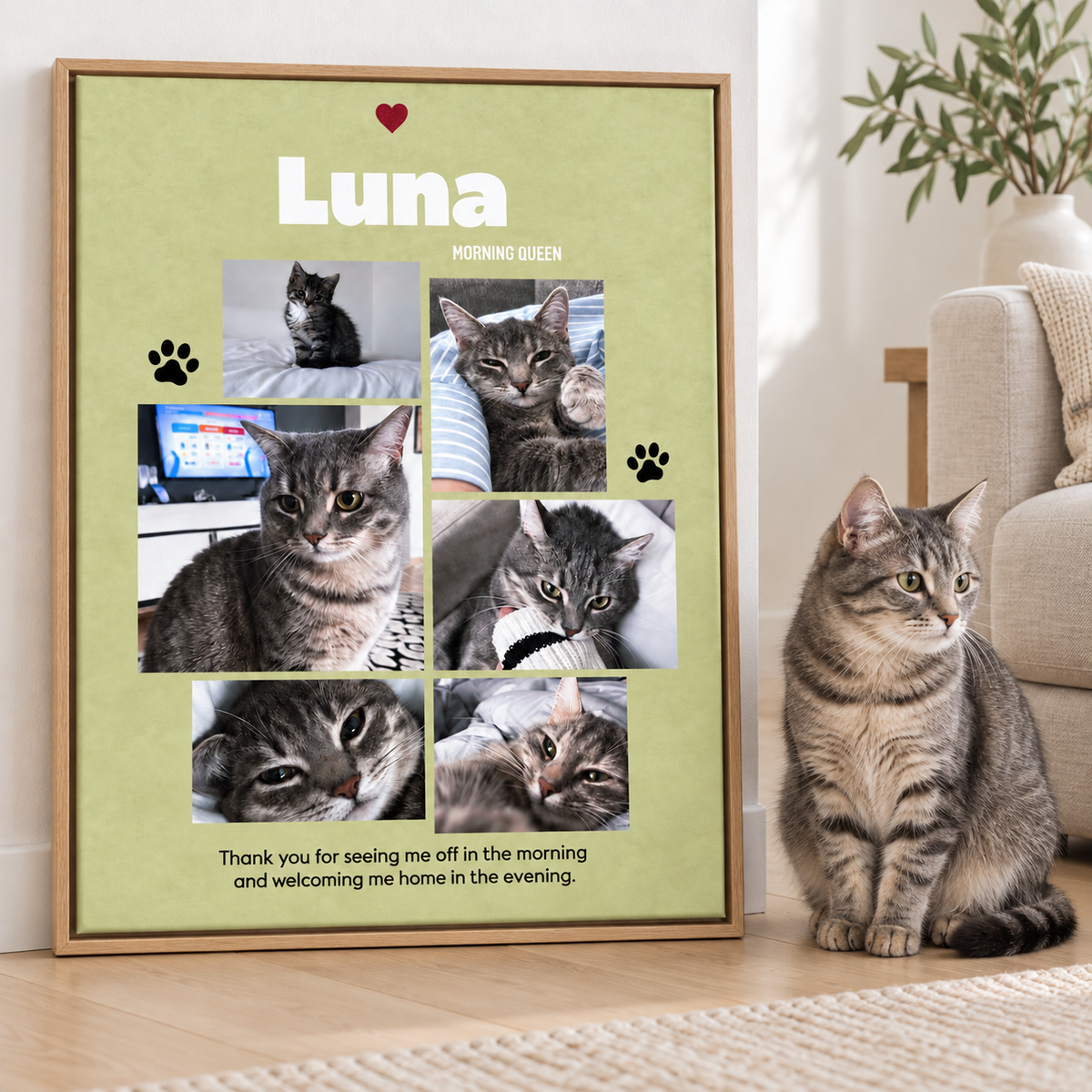 A framed personalized cat photo collage poster leaning against a wall on a wooden floor, next to a real tabby cat sitting on a rug in a living room. The poster is light green with the name 'Luna' at the top, several photos of the cat, paw prints, and a short message at the bottom.